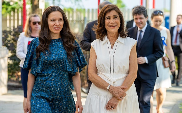 Mirabela Grădinaru zâmbitoare, imbracata cu rochie cu modele in nuante de albastru, mergand alaturi de sotia ambasadorului SUA in Romania, imbracata cu rochie alba fara maneca, in spatele lor aflandu-se Nicusor Dan si diversei oficiali de la Ambasada SUA