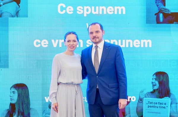 Mirabela Gradinaru zambitoare, imbracata in rochie deschisa la culoare, cu maneca lunga, alaturi de actualul ministru al Sanatatii, Alexandru Rogobete, imbracat cu costum albastru si camasa alba, amandoi stand cu spatele la un ecran pe care se deruleaza proiectul pentru adolescenti si tineri in care sunt implicati cei doi