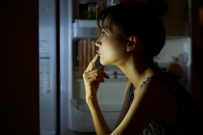 Femeie care se uita in frigider noaptea, gandindu-se ce sa manance