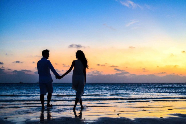 Cuplu care se plimba de mana pe plaja la apus