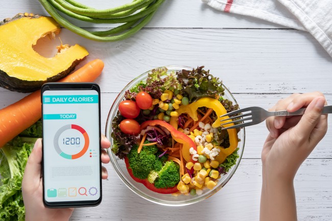 Aplicație de contorizare a caloriilor pe ecranul smartphone-ului la masa de luat masa cu salată, suc de fructe, pâine și legume proaspete