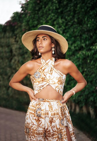 Femeie bronzata, cu palarie de soare pe cap, imbracata intr-un compleu cu maieu crop top si pantaloni evazati