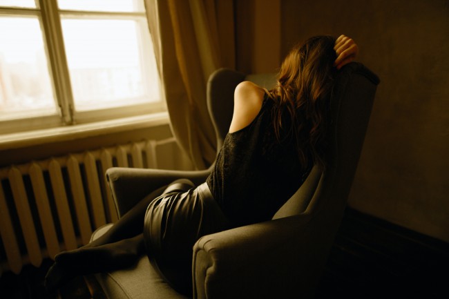 Femeie trista fotografiata de la spate, cuibarita pe un scaun