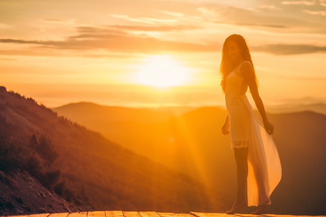 O femeie în rochie albă în picioare pe o scândură de lemn în timpul apusului de soare