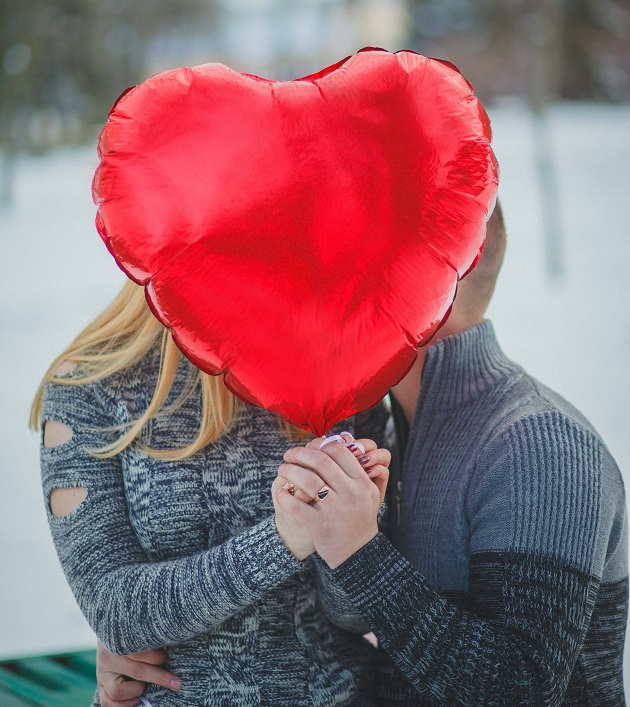 cuplu care se saruta in spatele unui balon in formă de inimă 