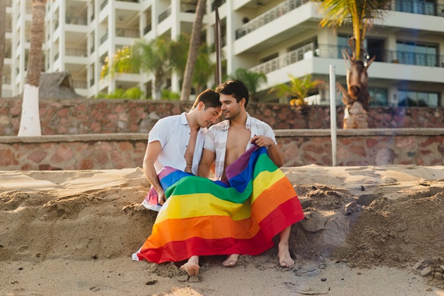 Cuplu gay pe o plajă cu un steag LGBT în mână