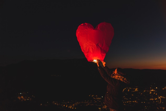 Persoană care ține în mână un balon în formă de inimă