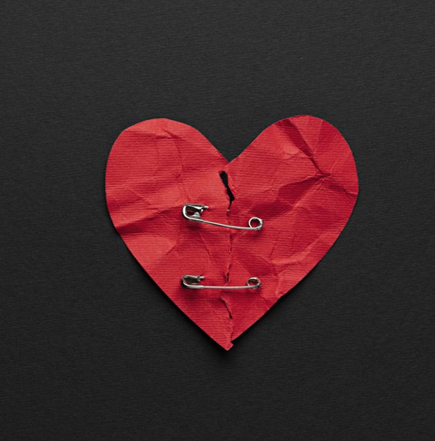 Fundal negru și o Inimă roșie, din hârtie, ruptă și prinsă cu ace de siguranță