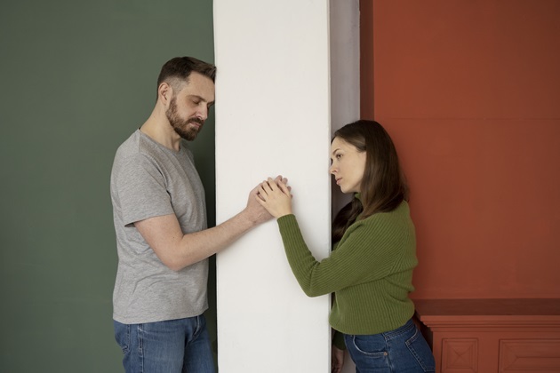 Cuplu cu probleme de comunicare, ambii parteneri ascunzându-se în spatele unui zid, însă continuând să se țină de mână