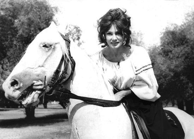 Actrița Marga Barbu călărind un cal alb, îmbrăcată într-o rochiță cu motive tradiționale