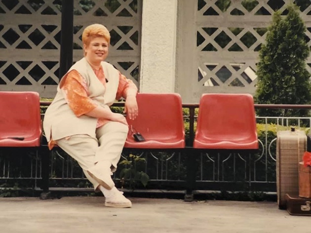 Poză veche cu Teo Trandafir asezată pe niste scaune roșii, îmbărcată într-un costum casual, in timpul unor filmări
