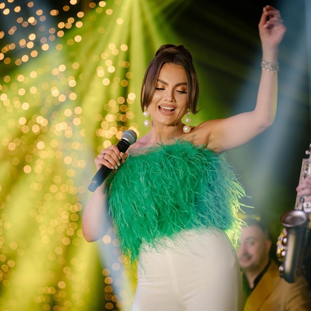 Irina Maria Birou pe o scena muzicala, in timpul unei filmari, purtând un top verde din pene 