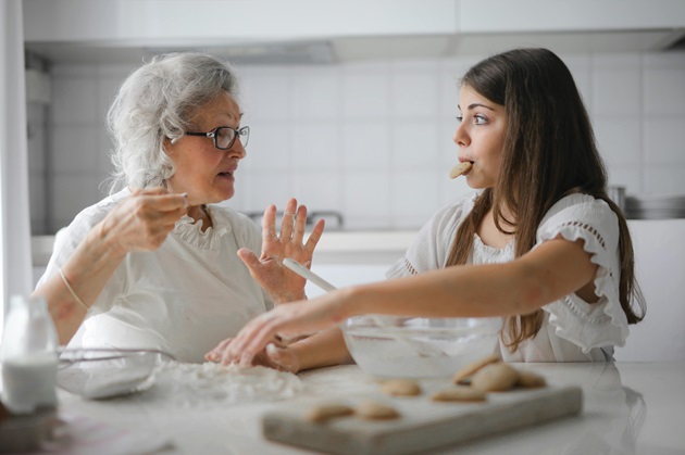 Două femei care vorbesc în timp ce pregătesc și mănâncă biscuiți
