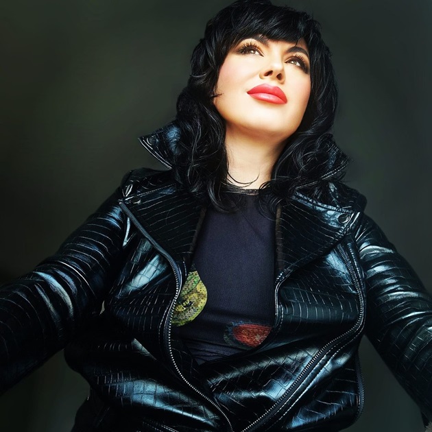 Mariana Moculescu cu privirea în sus, purtând o jachetă din piele neagră și o maletă cu detalii colorate