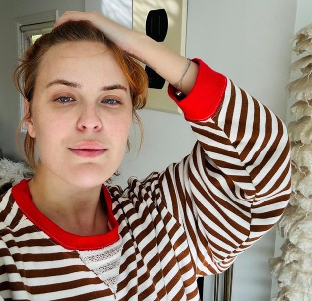 Tallulah Willis tinându-și o mâna în păr și purând o bluză în dungi albe și vișinii