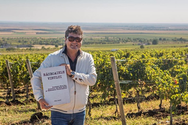 Cătălin Păduraru in fața unei podgorii de vin, ținând în mână o tăbliță personalizata