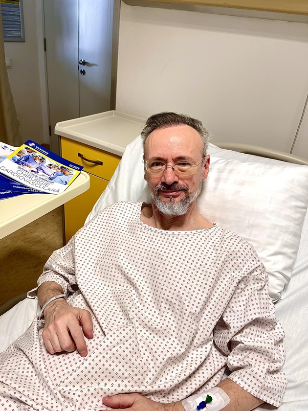 Mihai Albu îmbrăcat în cămașă albă cu romburi, pe patul de spital 