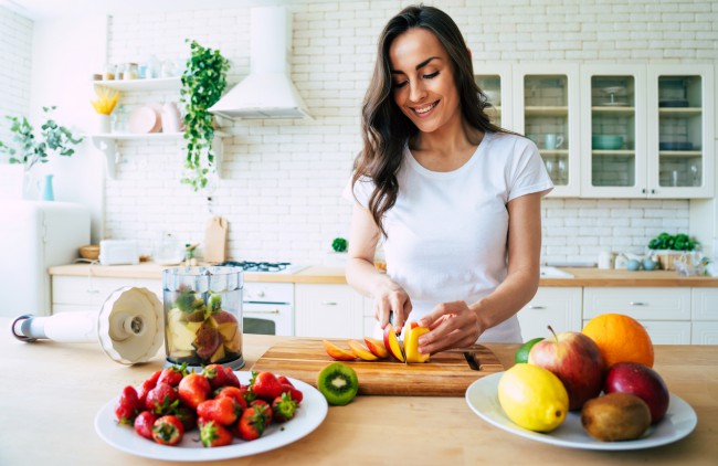 femeie tanara care taie fructe pentru a le pune in blender