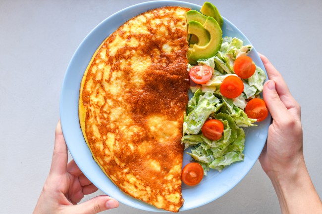 omleta impaturita servita cu avocado, rosii si salata verde pe un platou intins