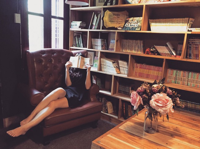 fata frumoasa care sta si citeste in biblioteca, decor cu carti si fotoliu de piele cu buchet de flori in prim plan