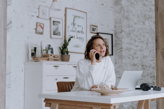 femeie care munceste la birou cu laptop in fata si vorbeste la telefon