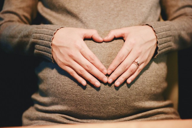 femeie insarcinata imbracata in rochie bej cu mainile impreunate pe pantece