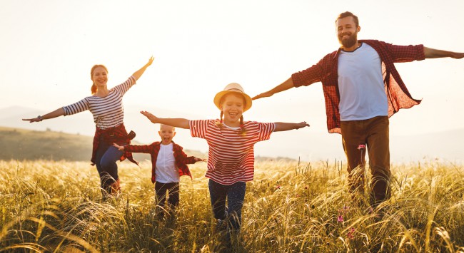 familie formata din mama, tata si copii alearga liberi pe un camp cu iarba