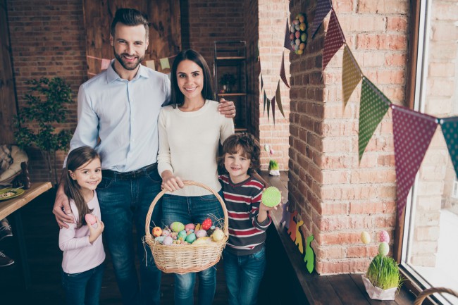 familie formata din mama, tata si copii in casa decorata festiv tin in mana un cos plin cu oua de paste