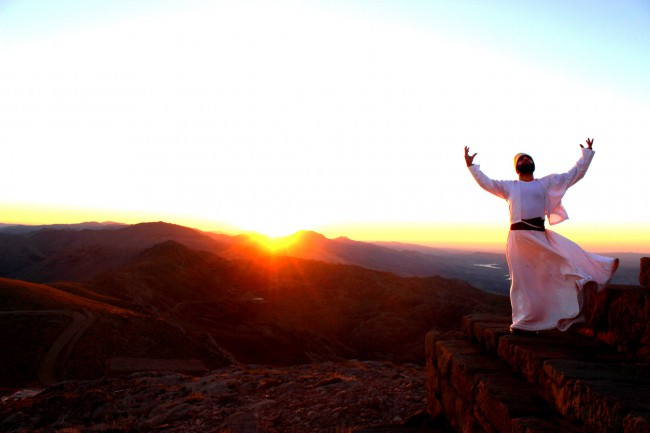 musulman imbracat in alb se roaga in munti cu soarele aparand la orizont
