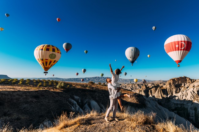 cuplu la munte care se imbratiseaza fericiti in timp ce in jurul lor zboara baloane umflate, Cappadocia, Turica