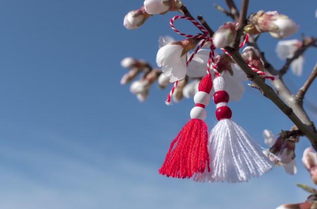 martisor cu margele albe si rosii atarnat de o ramura de copac inflorita