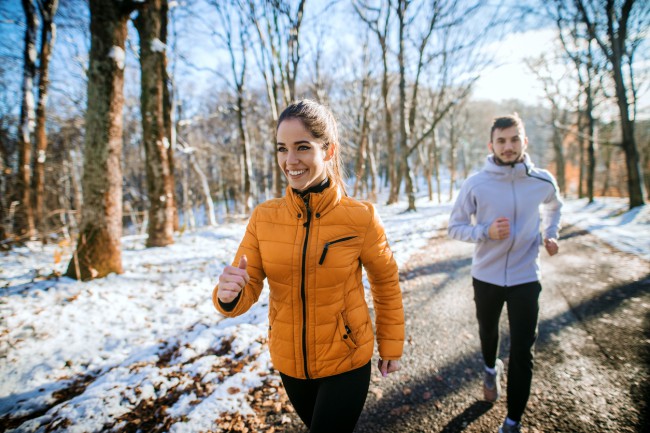 femeie si barbat care fac jogging fericiti intr-o padure insorita pe timp de iarna