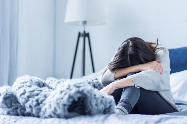 femeie trista si depresiva care sta in pat cu capul plecat si patura groasa in prim plan; simptome lipsa de fier