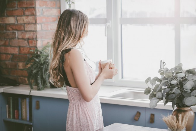 femeie frumoasa si blonda care bea ceai in fata ferestrei in bucataria plina de plante