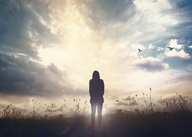 femeie aflata pe un camp pustiu priveste la cerul luminat si la pasari, concept sanatate mintala, rugaciune si credinra