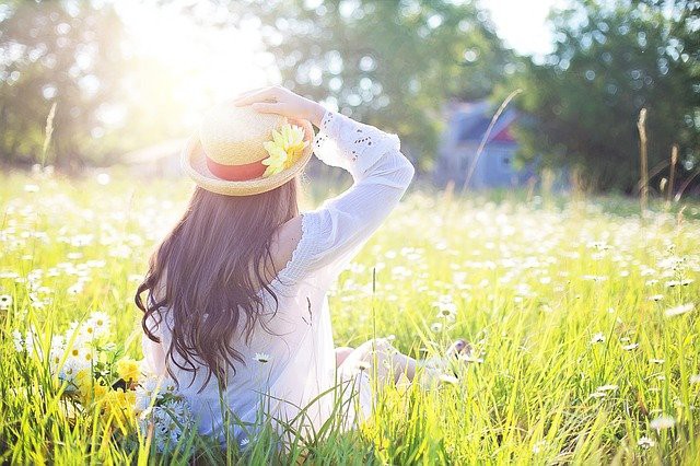 femeie cu palarie care sta pe un camp verde plin cu flori la soare