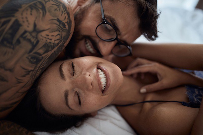cuplu care sta in pat, fata indragostita si baiat tatuat care se imbratiseaza in pat