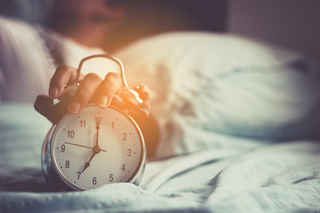 femeie obosita in pat care opreste alarma de la ceas
