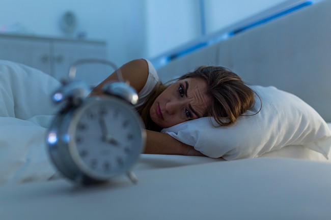 femeie obosita in pat care se uita disperat la ceas
