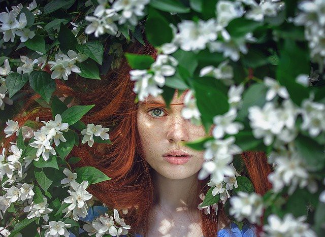 femeie roscata care priveste printre flori de primavara