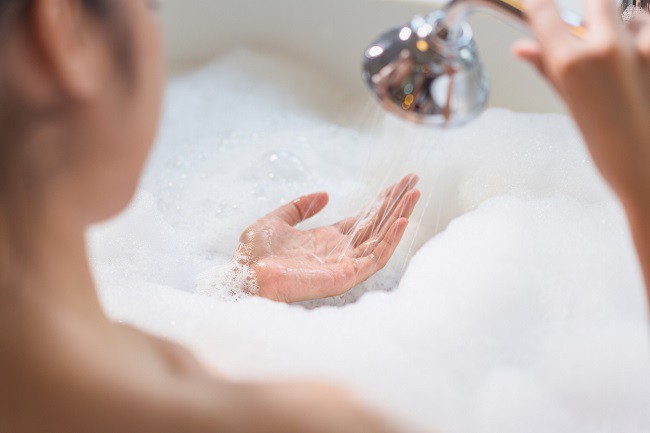 femeie care isi face baie in cada plina cu spuma si pune apa in palma