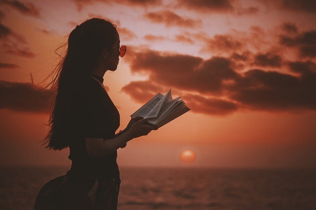fata tanara care citeste dintr-o carte in lumina unui asfintit la mare