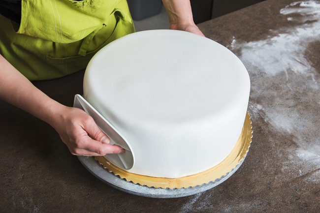 mana de femeie care decoreaza un tort cu glazura alba