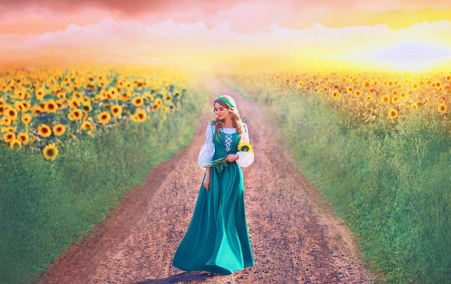 femeie imbracata in port national se plimba printre flori de floarea soarelui