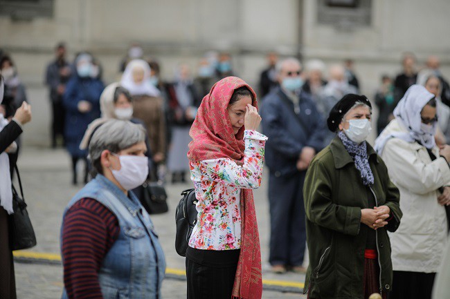 credinciosi cu masca care se inchina in fata bisericii