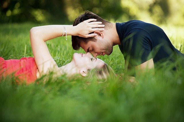 femeie blonda si barbat indragostit care se saruta in iarba