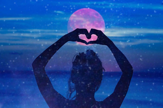 femeie cu mainile ridicate se uita la o luna roz pe fundal albastru