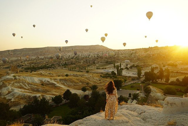 femeie imbracata in rochie aflata la munte in cappadocia care se uita la soare ce apune 