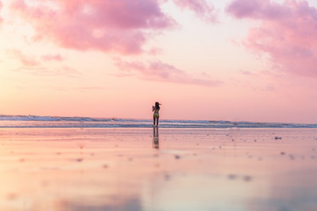 fata care sta singura in apropierea asfintitului la tarmul unui ocean roz