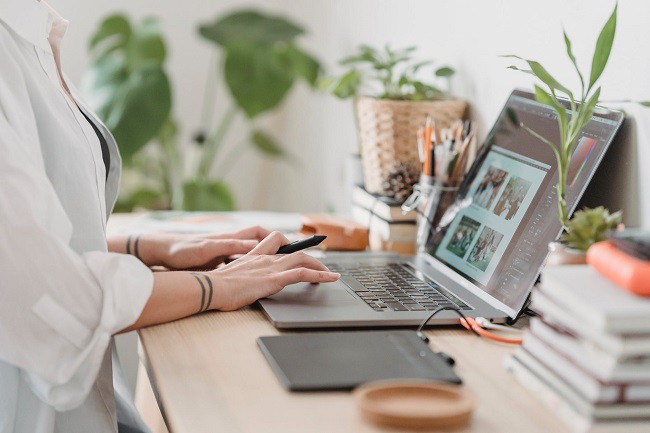 femeie care lucreaza la laptop la un birou aranjat cu plante